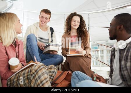 Multi-ethnic group of students sitting on stairs in college and chatting while working on homework Stock Photo