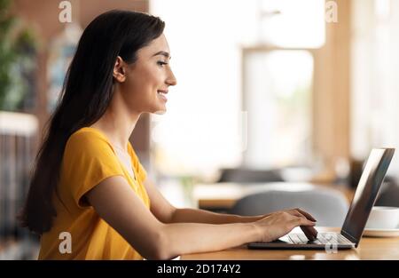Smiling arab woman using laptop while sitting at cafe Stock Photo