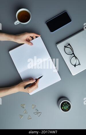 Above view background of female hands writing or sketching in blank white planner while working on grey workplace, copy space Stock Photo