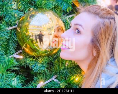 A woman's profile and his reflection in a golden Christmas ball hanging on a tree Stock Photo