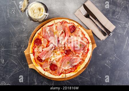 Pizza with salami and prosciutto on wooden board on dark background Stock Photo