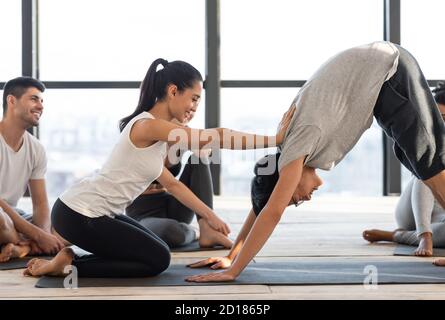 Professional female yoga instructor correcting group member during group training in studio Stock Photo