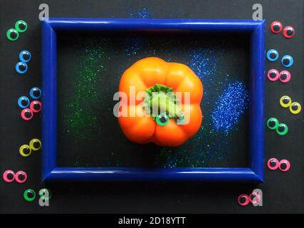 Creative Autumn Halloween layout made of colorful plastic eyes, an orange pepper in a blue frame on a black background with tinsel Stock Photo