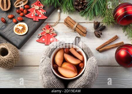 Happy New Year and merry Christmas, mittened hands holding a mug of mulled wine with fruit and cinnamon on a white background with Christmas toys. Stock Photo