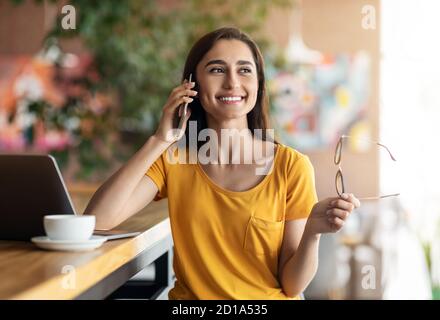 Happy female student talking on phone while studying at cafe Stock Photo