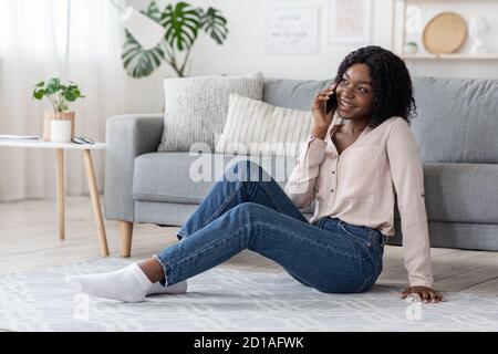 Home Pastime. Cheerful african lady woman talking on cellphone in living room Stock Photo