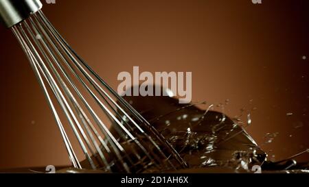 Freeze motion of wire whisk rotating hot melted chocolate, isolated on soft gradient background Stock Photo