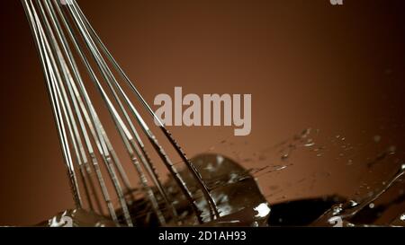 Freeze motion of wire whisk rotating hot melted chocolate, isolated on soft gradient background Stock Photo