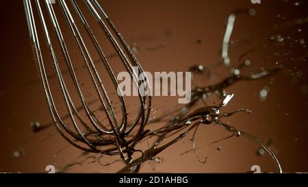 Freeze motion of wire whisk rotating hot melted chocolate, isolated on soft gradient background Stock Photo
