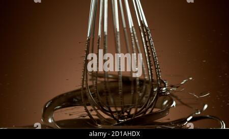 Freeze motion of wire whisk rotating hot melted chocolate, isolated on soft gradient background Stock Photo
