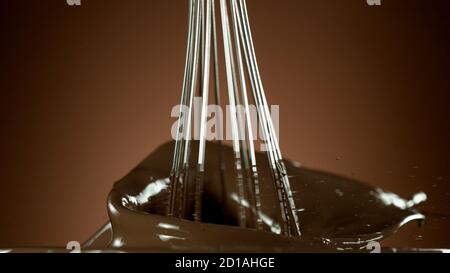 Freeze motion of wire whisk rotating hot melted chocolate, isolated on soft gradient background Stock Photo