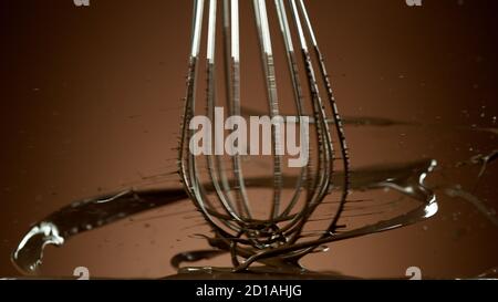 Freeze motion of wire whisk rotating hot melted chocolate, isolated on soft gradient background Stock Photo