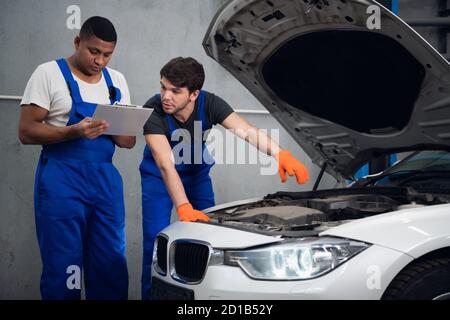 Two mechanics inspect the engine of a vehicle and discuss repair Stock Photo