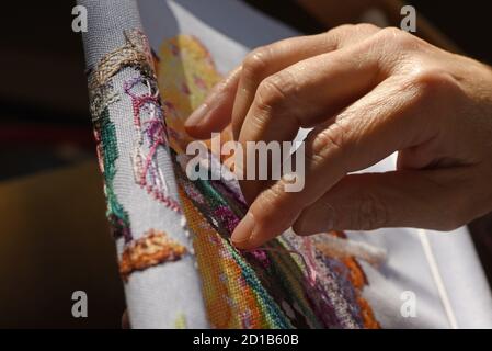 A woman cross stitches a cross stitch pattern by Mirabilia on an evenweave fabric Stock Photo