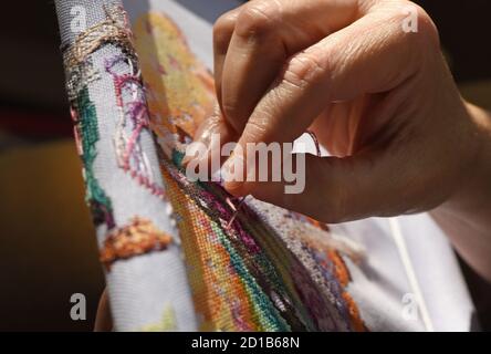 A woman cross stitches a cross stitch pattern by Mirabilia on an evenweave fabric Stock Photo