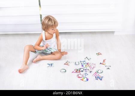 Beautiful little boy learning letters on the floor at home. Stock Photo