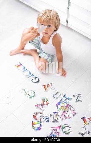 Beautiful little boy learning letters on the floor at home. Stock Photo