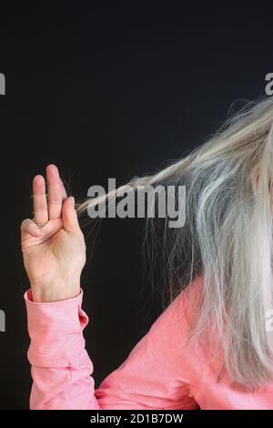 Close up of a woman in her 60s holding a strand of grey hair. Stock Photo