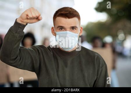 Guy in face mask gesturing over group of demonstrators Stock Photo