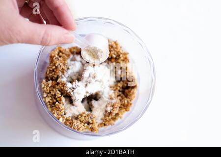 step by step visual instruction how to make energy balls. step 2, add protein powder to the mix of nuts and fruits. protein balls making. hand holding scoop of collagen Stock Photo