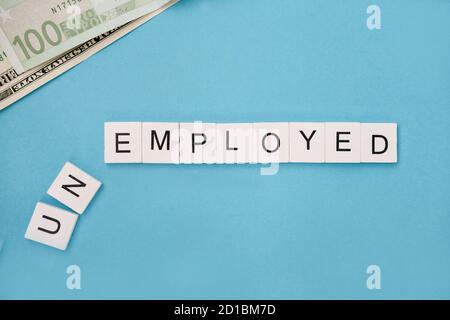 unemployed spelled out in wooden letter tiles on a blue background, copy space for ad text. unemployment concept. global financial crisis. Stock Photo
