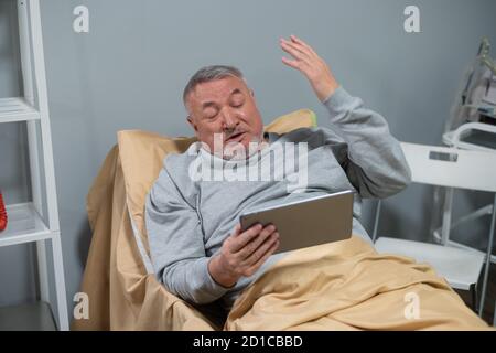 A senior man watching sports games on his tab, he is not happy with the way his team is playing today. Stock Photo