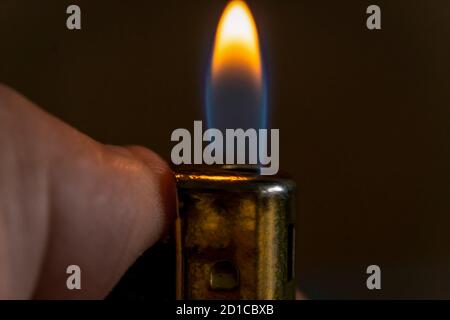 Hand holding a burning lighter in the dark, macro photo. Background with fire Stock Photo