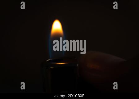 Hand holding a burning lighter in the dark, macro photo. Background with fire Stock Photo