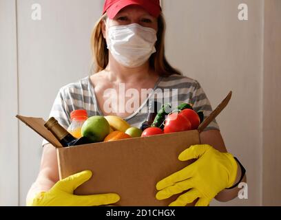 Safe shopping in pandemic. woman Courier wearing face mask, gloves delivering grocery order in coronavirus epidemic. Food delivery during corona virus outbreak. Takeout meal. People stockpile food.  Stock Photo