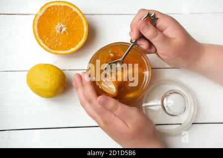 teenager's hands holding a spoon with orange and lemon jam. homemade orange marmalade. breakfast in rustic style. autumn harvesting and making jelly. top view.  Stock Photo