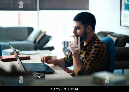 Man Working From Home With Computer And Smoking Cigarette Stock Photo