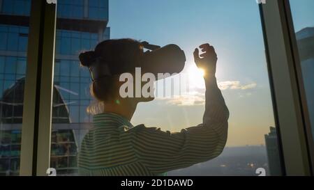VR, sightseeing, discover, technology concept. Woman using virtual reality headset and moving hand against view on cityscape from panoramic skyscraper Stock Photo