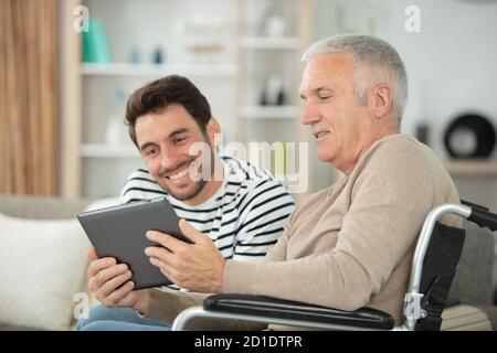 happy handsome father in wheelchair and son using tablet Stock Photo