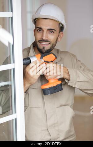 smiling man fixing a window handle using cordless screwdriver Stock Photo