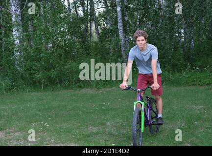 teenager boy riding a bike in a park. curly teenager on a bicycle. active sport outdoors.  Stock Photo