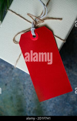 Gift box with empty red card, surrounded by pine branches rustic blue background. Closed gift for Christmas celebration at home Stock Photo