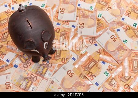 Conceptual. Piggy bank to introduce small savings on a pile of fifty euro bills Stock Photo