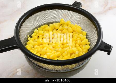 Freshly rinsed canned corn kernels draining in strainer in bowl on table Stock Photo
