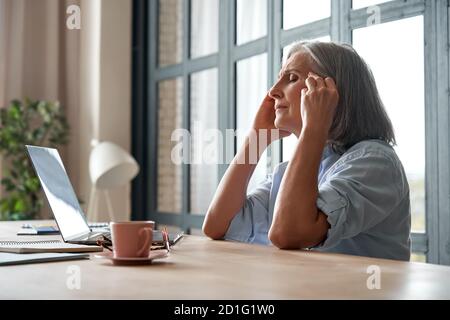 Stressed overworked old mature business woman suffering from headache at work. Stock Photo