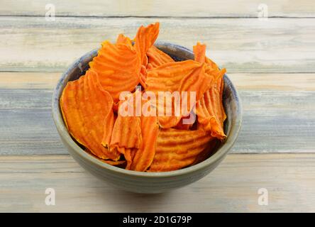 Organic sweet potato chips in ceramic snack bowl on table Stock Photo