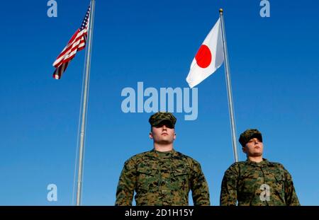 U.S. Marines walk past the U.S. and Japanese national flags at Marine headquarters at Camp Foster in Ginowan, southern Japanese island of Okinawa, March 6, 2008. Once an independent kingdom with a rich culture and its own language, Okinawa has long been trapped in a strategic triangle with Washington and Tokyo, 1,600 km (1,000 miles) to the north. One third of its population was killed in the bloody Battle of Okinawa in the final months of World War Two, after which the island was occupied by the United States until 1972. Picture taken March 6, 2008. To match feature JAPAN-USA/OKINAWA    REUTE