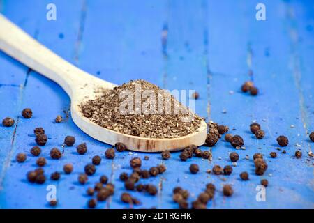 Close-up of black pepper powder in wooden spoon and black peppercorns on wooden blue background. selective focus. Stock Photo