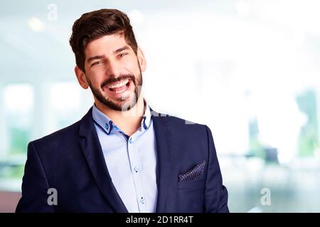 Portrait shot of young businessman wearing suit and looking at camera while standing indoor and smiling. Stock Photo