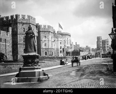 WINDSOR CASTLE, Berkshire. View from the junction of High Street and Peascod Street looking along Castle Hill with the statue of Queen Victoria in the foreground. A large group of soldiers in bearskins has congregated in front of the gates, watched by a group of onlookers. Photographed in 1888 by Henry Taunt. Stock Photo