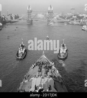 TOWER BRIDGE, Stepney, London. Looking down onto the foredeck of the cruiser HMS Belfast. Being guided up the River Thames by two tugs on the approach to Tower Bridge, which is opening to let it pass. This was Belfast's last voyage before she moored in the Pool of London. It was there converted to a static visitor attraction and is now operated by the Imperial War Museum. Photographed by Eric de Mare in 1971. Stock Photo