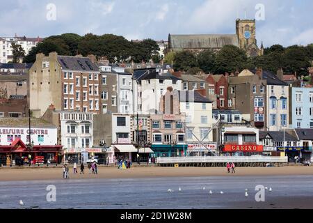 General view looking north-west from the beach towards shops, cafes and amusement arcades at the north end of the street, with St Mary's Church in the background, Scarborough, North Yorkshire, UK.