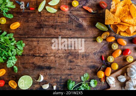 Lime, cilantro, chili, nachos background with copy space. Ingredients for Pico de gallo Salsa sauce or other mexican or latin american food. On a rust Stock Photo