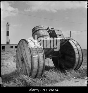 Dungeness, Lydd, Shepway, Kent. A horse-drawn cart loaded with beer crates and a barrel on display in the car park beside Dungeness Old Lighthouse, with the new lighthouse visible in the background. Stock Photo