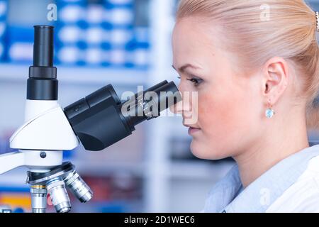 Girl with a slide for the microscope University Hospital. Attractive young scientist  looking at the microscope slide in the forensic laboratory Stock Photo