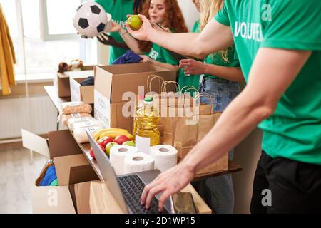 group of diverse people sort through donated food items while volunteering in community, they use cardboard boxes for collecting donation Stock Photo